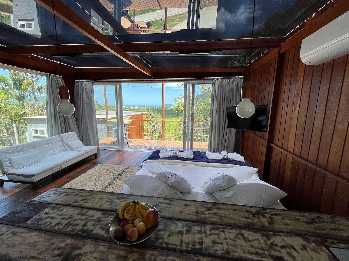 A bedroom with a bed, a sofa, a fruit bowl, and a view of the outdoors.