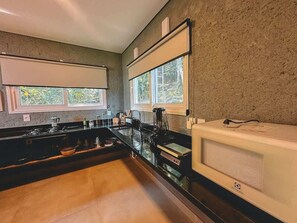 Una cucina moderna con piano di lavoro nero, forno a microonde integrato e una finestra vista verde.