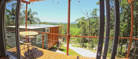 A modern outdoor deck with a wooden floor, a glass enclosure, and a table with chairs.