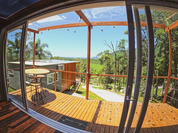 A modern outdoor deck with a wooden floor, a glass enclosure, and a table with chairs.