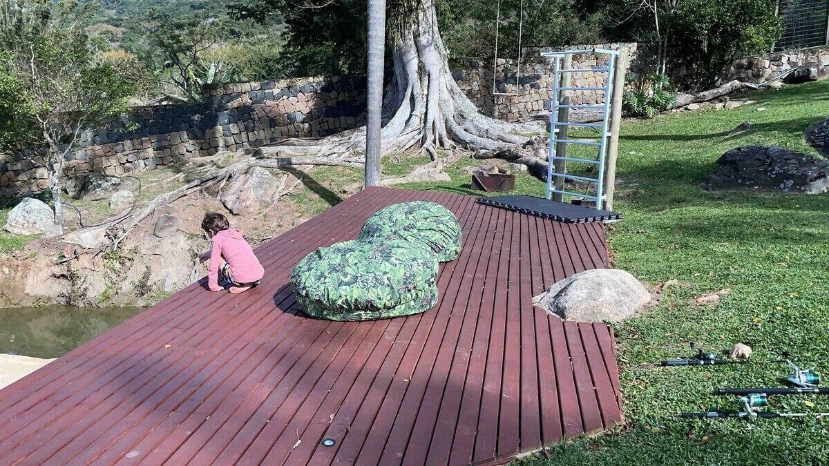 A wooden deck with a person sitting on a green cushion, a ladder, and a stone wall in the background.