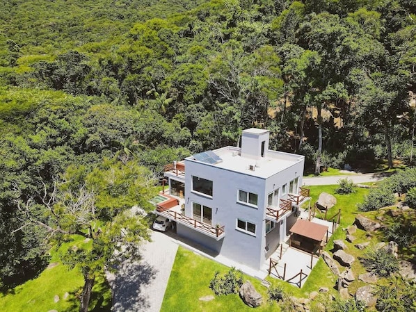 A modern two-story house with a flat roof, surrounded by lush greenery and a well-maintained lawn.