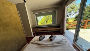 Een slaapkamer met een groot bed, een raam met uitzicht op groen en een houten bankje.