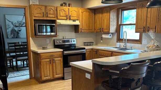 A modern kitchen with wooden cabinets, a central island with bar stools, a microwave, and a stove. - Backyard bliss/firepit/spacious/cozy/centrally located (Wichita)