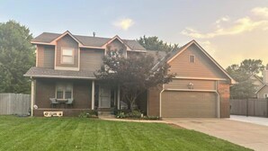 A two-story house with a front porch, a garage, and a well-maintained lawn. - Backyard bliss/firepit/spacious/cozy/centrally located (Wichita)