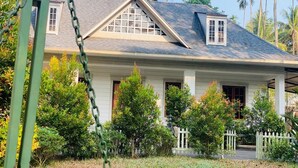Et toetagers hus med en veranda, omgivet af frodig vegetation og palmer.