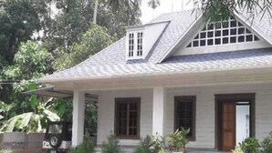 Uma casa de dois andares com fachada branca, telhado inclinado e uma pequena varanda com colunas.