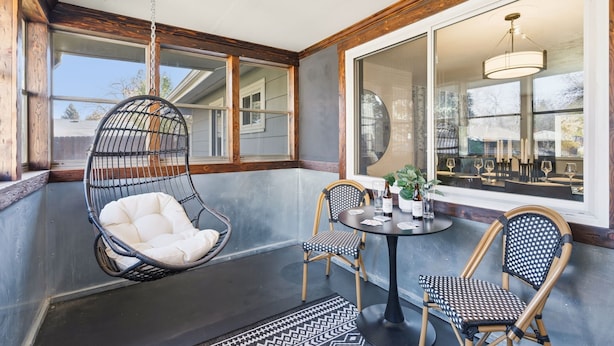 A cozy outdoor seating area with a hanging chair, two chairs, and a table with drinks.