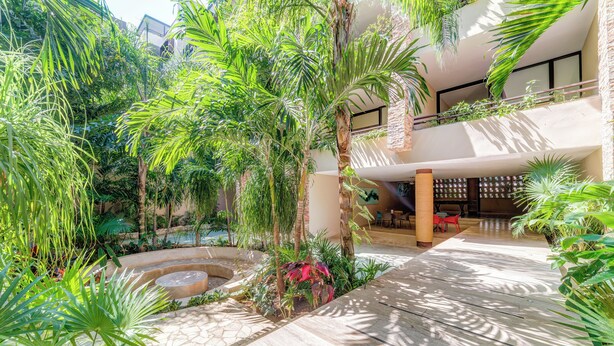 A modern hotel interior with a central courtyard, outdoor seating, and lush greenery. - Syrena Living Condos (Playa del Carmen)