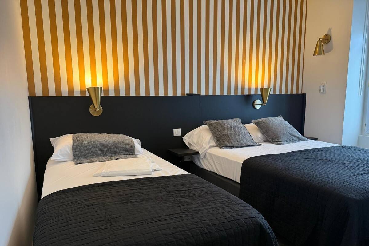 Una habitación de hotel con dos camas, papel tapiz a rayas y lámparas fijadas a la pared.