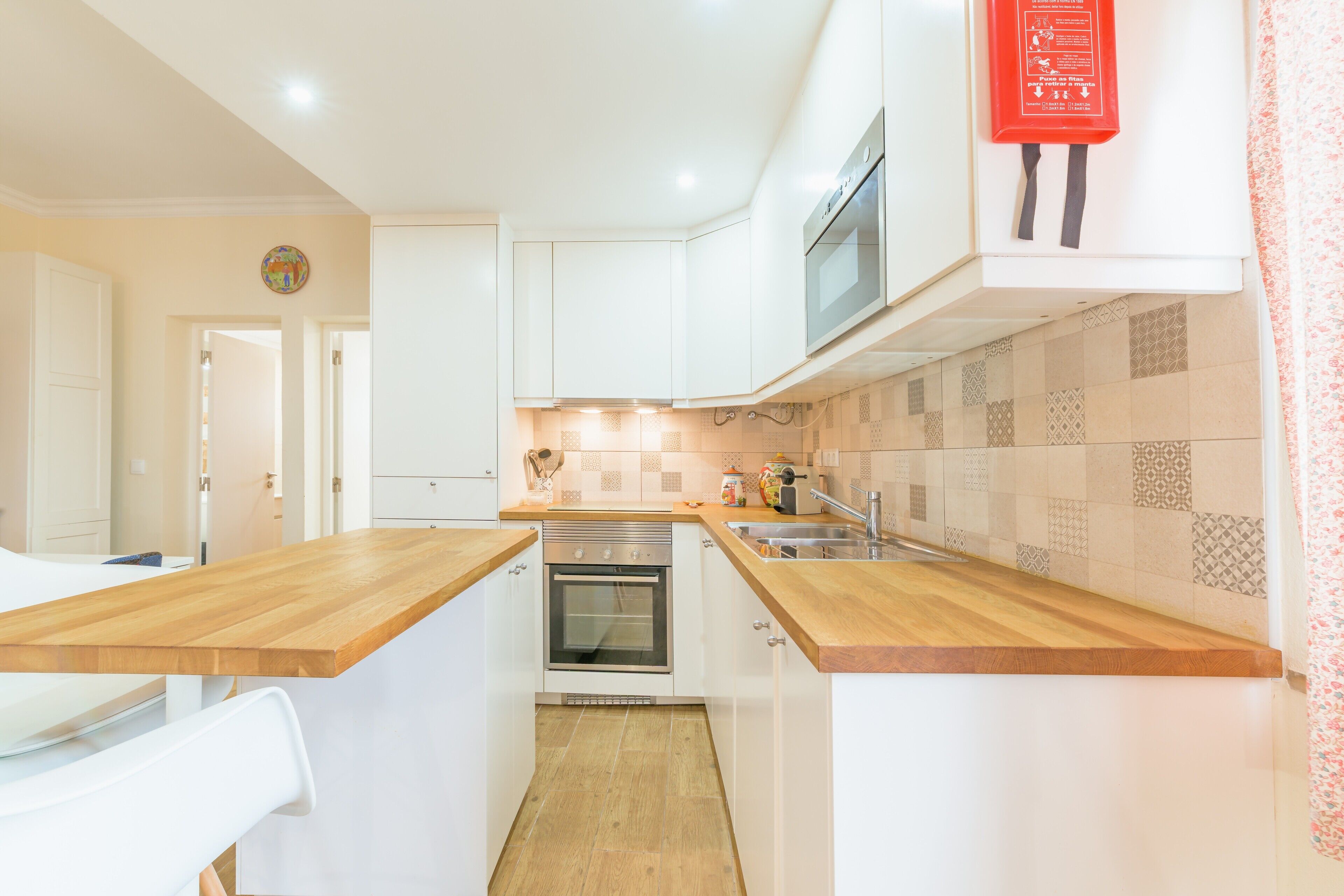 A compact kitchen with white cabinets, a wooden countertop, a built-in oven, and a microwave.