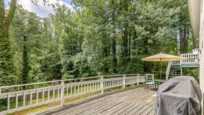 Een houten terras met een witte balustrade, een overdekte barbecue en een zonnescherm.