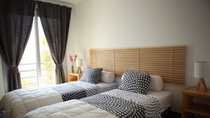 Camera d'albergo con due letti, una testiera in legno, un comodino con una lampada e una finestra con tende.