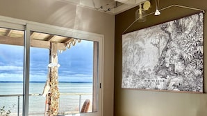Una habitació amb un escriptori de fusta, un gran finestral amb vista a la platja i una obra d'art penjada a la paret.