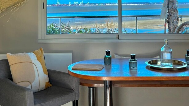 Habitació amb vista al mar, taula rodona amb safata, una cadira i una làmpada penjant.