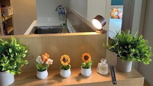 A kitchen counter with four potted plants and a bottle, a sink, and a mirror reflecting a teddy bear and a plant. - Villa Ratchatewi 5 STARS suite l 4 mins walk BTS&APL (Bangkok)