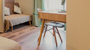 A room with a wooden desk, a chair, a bed with a headboard, a small table, and a lamp.