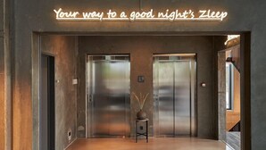 Un espace près des ascenseurs, agrémenté d’un panneau néon sur lequel on peut lire : « Pour passer une bonne nuit de sommeil », et d’une petite table sur laquelle est posé un vase.