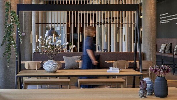 Un intérieur moderne avec un coin salon, un grand vase rempli de fleurs et une personne qui marche.