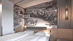 Une chambre moderne avec un grand lit, une tête de lit dotée d’un éclairage intégré et une œuvre d’art représentant une voiture de course, accrochée au mur.