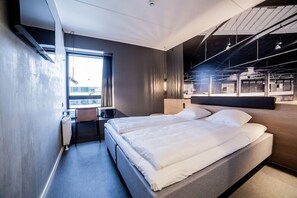 A modern hotel room with a large bed, a desk, and a view of the city.