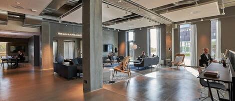 A spacious, modern office with a mix of seating areas, a long table for meetings, and large windows providing natural light.