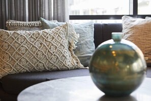 A modern living room with a sofa adorned with patterned cushions, a round table, and a decorative vase.