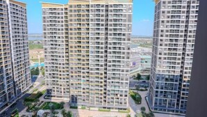 A high-rise residential building with multiple balconies, a central courtyard, and a view of the surrounding cityscape. - Beautiful Hotel at Vinhomes Grand Park (Ho Chi Minh City)