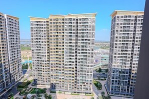 A high-rise residential building with multiple balconies, a central courtyard, and a view of the surrounding cityscape. - Beautiful Hotel at Vinhomes Grand Park (Ho Chi Minh City)