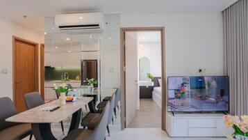 A modern living room with a flat-screen TV, a dining area with a table and chairs, and a kitchen in the background.