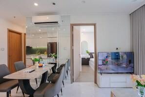 A modern living room with a flat-screen TV, a dining area with a table and chairs, and a kitchen in the background. - Beautiful Hotel at Vinhomes Grand Park (Ho Chi Minh City)