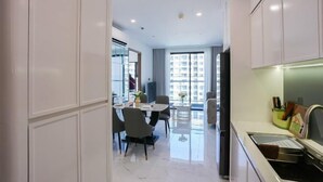 A modern kitchen with white cabinets, a dining area with a table and chairs, and a large window providing natural light. - Beautiful Hotel at Vinhomes Grand Park (Ho Chi Minh City)