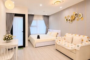A bedroom with a bed, a sofa, a table with a vase, and curtains. - Beautiful Hotel at Vinhomes Grand Park (Ho Chi Minh City)
