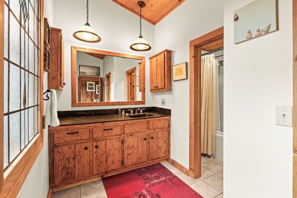 Une coiffeuse en bois avec un grand miroir, deux lampes suspendues et un tapis rouge dans une salle de bain.