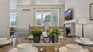 A dining area with a wooden table set for four, potted plants, and a fireplace in the background.