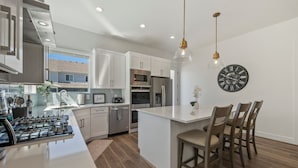 A modern kitchen with white cabinetry, stainless steel appliances, and a central island with bar stools.