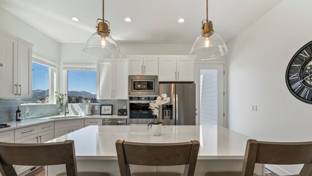 A modern kitchen with white cabinetry, stainless steel appliances, and a large island with three chairs.