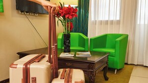 A room with two large suitcases, a television, a lamp, a green chair, and a vase with red flowers. - Amazonia de Saint-Laurent (Saint Laurent du Maroni)