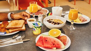 A breakfast setting with toast, croissants, a bowl of cereal, a glass of orange juice, and a plate with watermelon and grapefruit slices. - Amazonia de Saint-Laurent (Saint Laurent du Maroni)