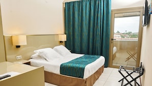 A hotel room with a bed, bedside lamps, a desk, a chair, and a view through a glass door. - Amazonia de Saint-Laurent (Saint Laurent du Maroni)