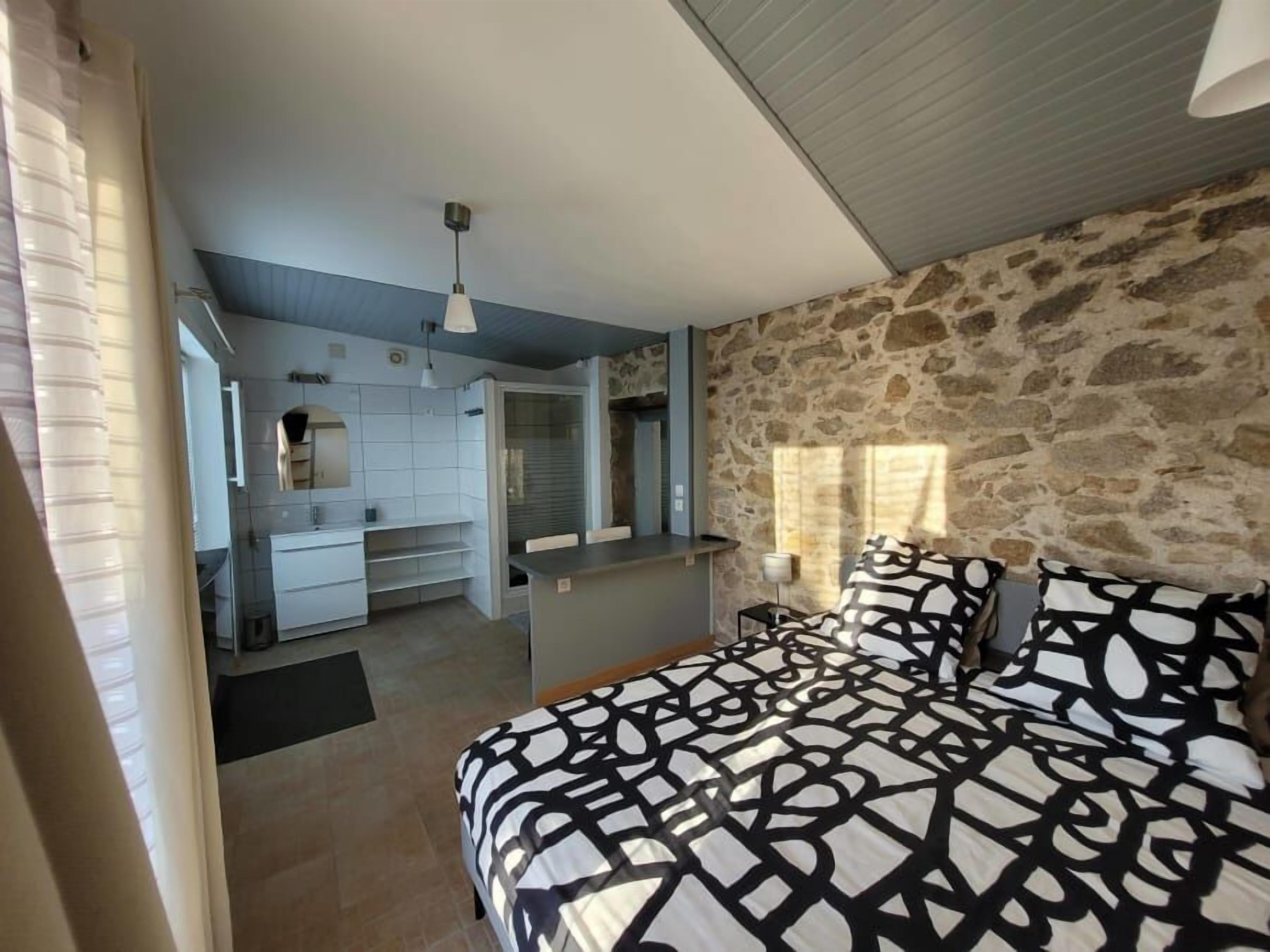 A bedroom with a bed, a stone wall, and a kitchenette.