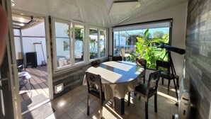 Un espace repas comprenant une table et des chaises, de grandes fenêtres et une vue sur la verdure environnante.