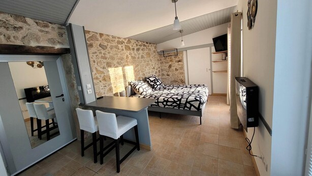 Une chambre à coucher de taille réduite, comprenant un lit, un bureau avec des chaises, une télévision et un mur en pierre.