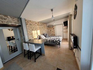 Une chambre à coucher de taille réduite, comprenant un lit, un bureau avec des chaises, une télévision et un mur en pierre.