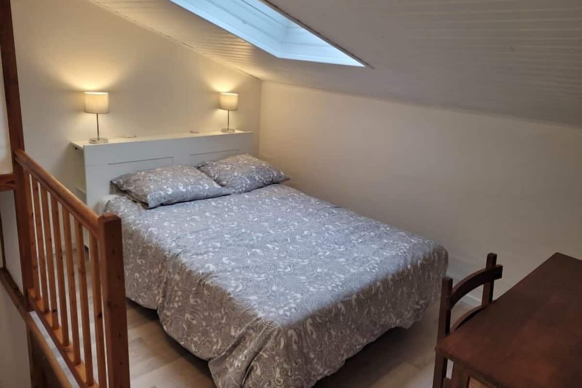 A bedroom with a skylight, a bed with patterned bedding, two bedside lamps, and a wooden chair.