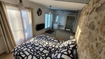 Une chambre avec un lit, une télévision, une salle de bain et un mur en pierre.