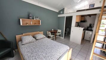 Ein Schlafzimmer mit Bett, Schreibtisch und Stuhl. Anliegend befindet sich eine Küchenzeile.