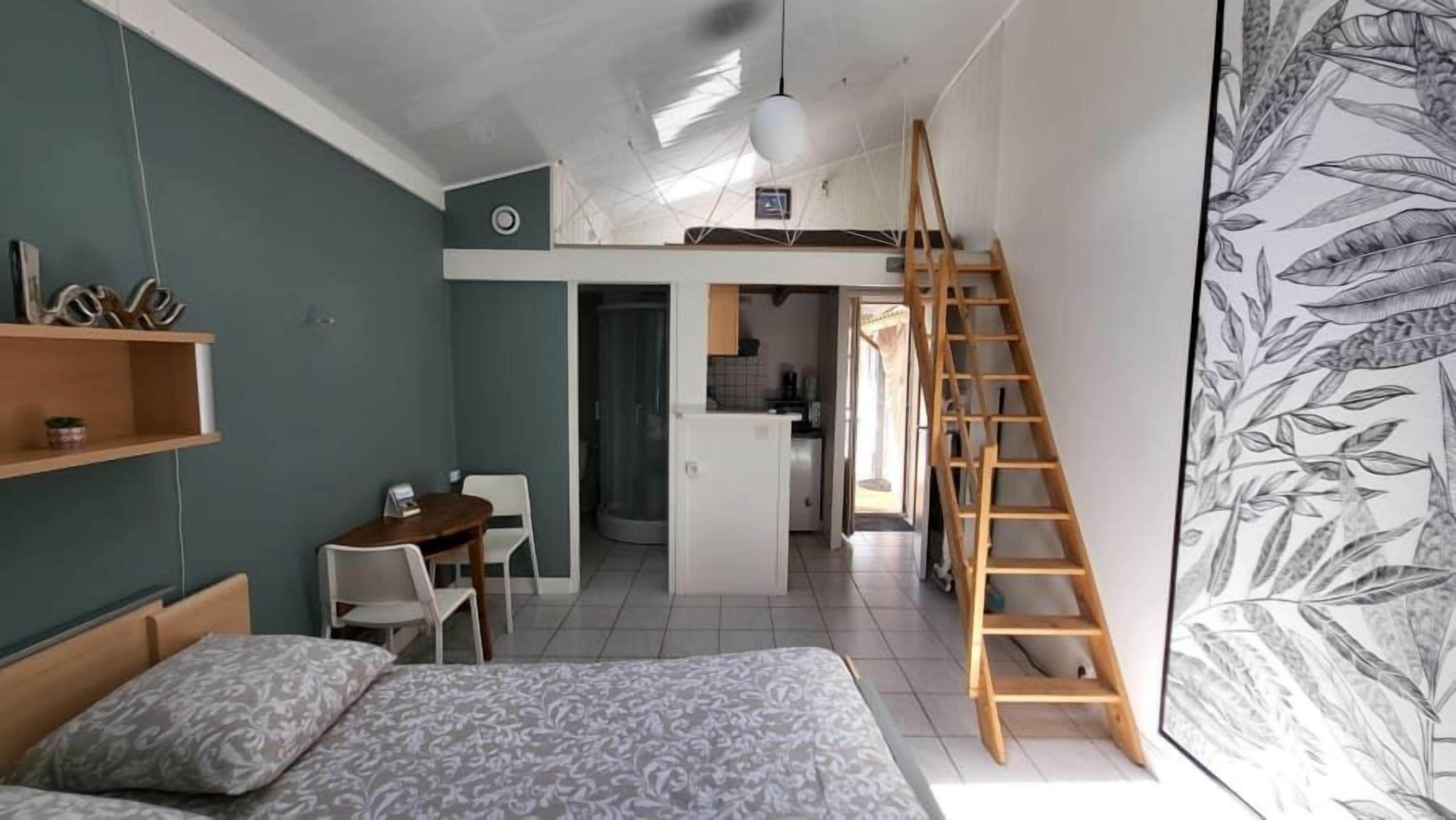 Een compacte slaapkamer met een bed, een bureau en een stoel. Er is een houten trap die naar een hoger niveau leidt.