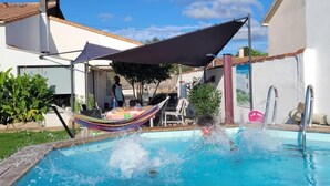 Un jardin avec une piscine, un hamac et un espace patio couvert.