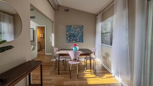 A dining area with a wooden table and six chairs, a painting on the wall, and a window with blinds. - The Loft at Raintree (Lakeland)